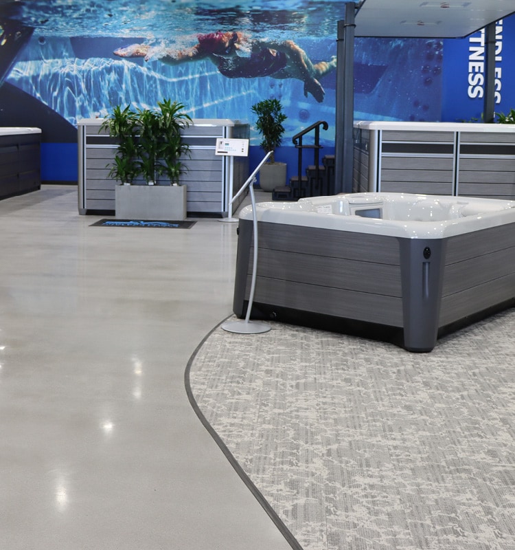 Inside the Danvers showroom featuring a large endless pools display wall with a woman swimming laps. Inf front of that are three Endless pools, and a hot tub.