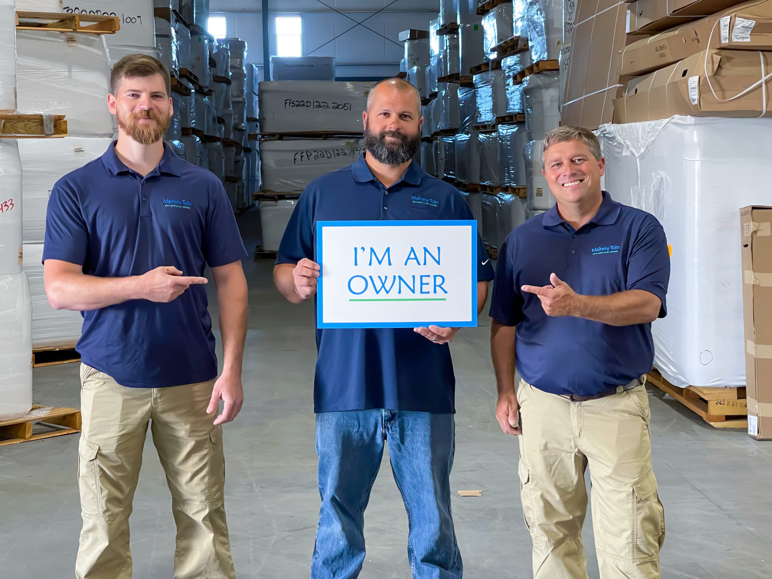 Three service technicians inside a warehouse, one in the middle holding 'I'm an owner sign.'