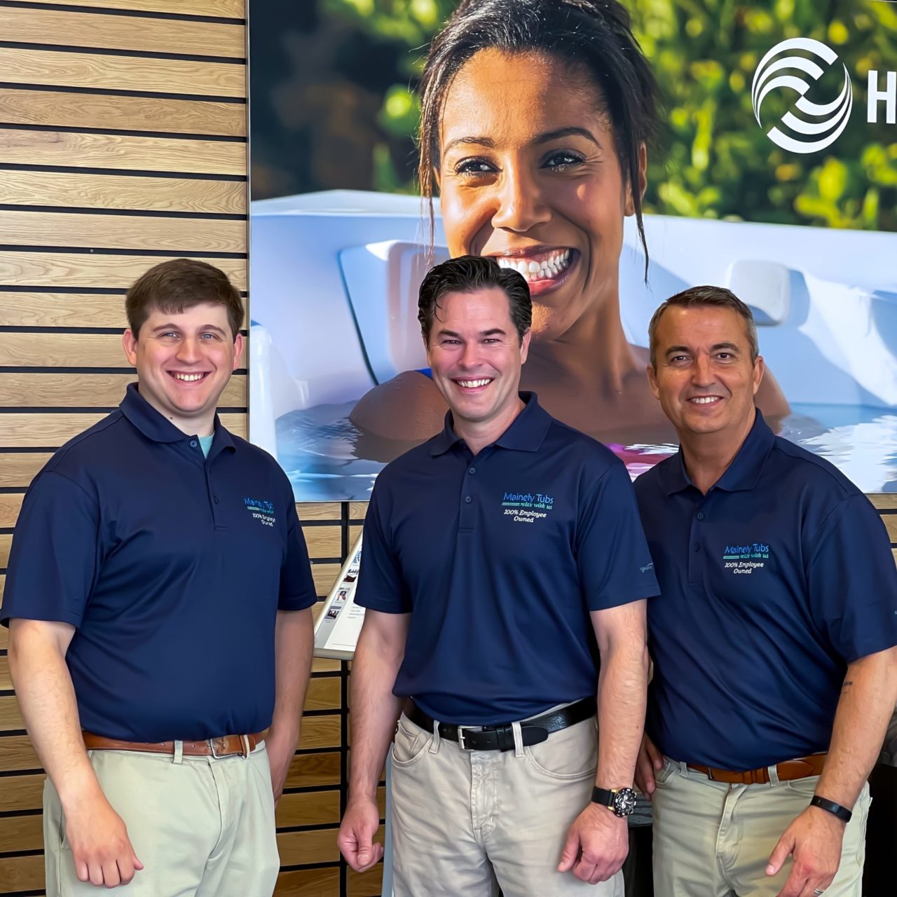 Three salespeople in front of a wall with a HotSpring sign in the Danvers showroom. 